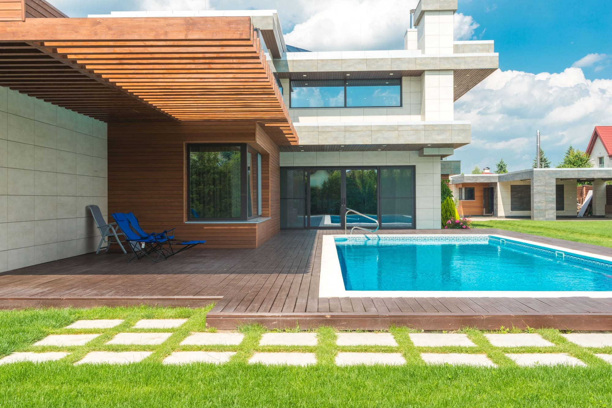Modern house with pool, wooden deck, and contemporary architecture featuring blue loungers