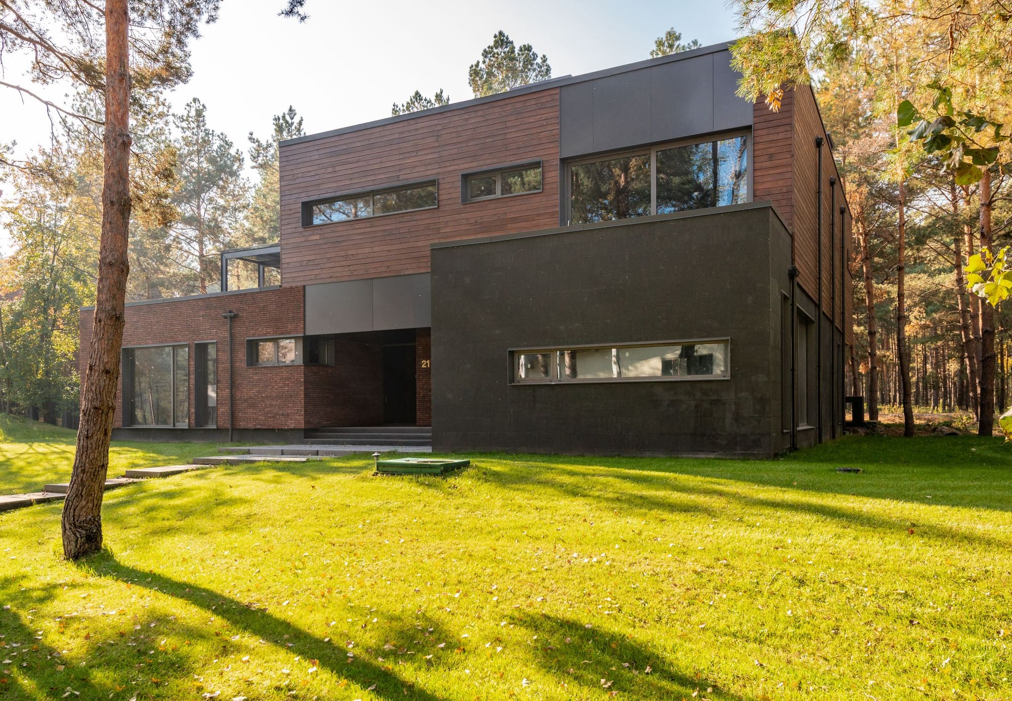 Modern two-story residential home with brick and wood siding surrounded by tall pine trees and green lawn