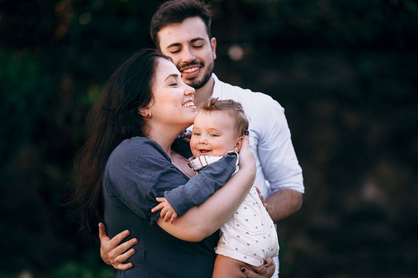 Happy family of three smiling outdoors in natural setting with blurred green background
