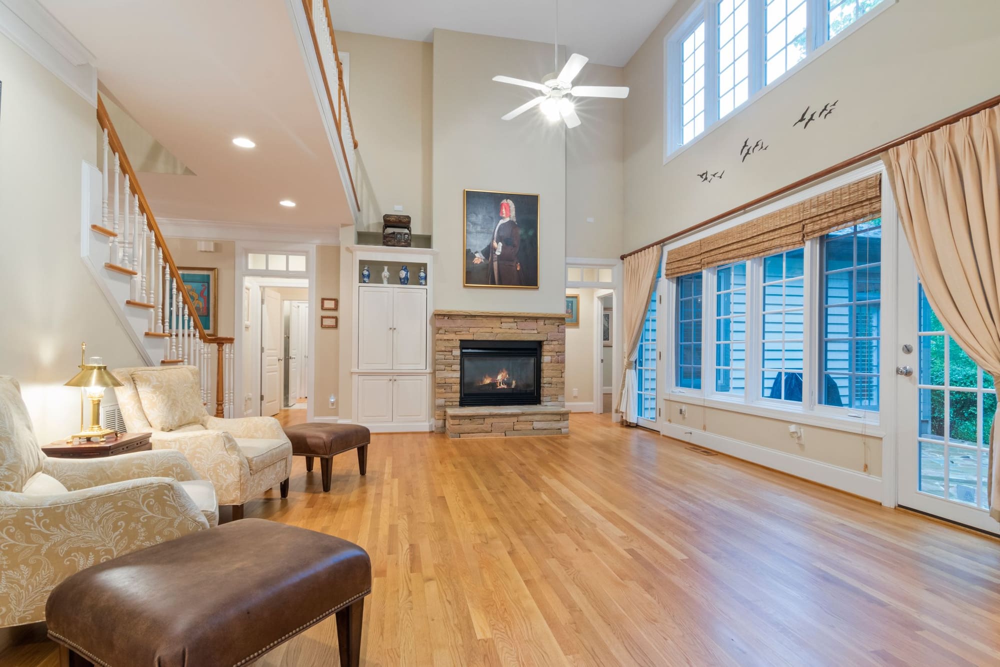 Spacious living room with fireplace, hardwood floors, ceiling fan, and large windows with shutters